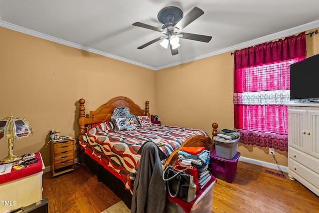 bedroom with wood finished floors, visible vents, baseboards, a ceiling fan, and crown molding