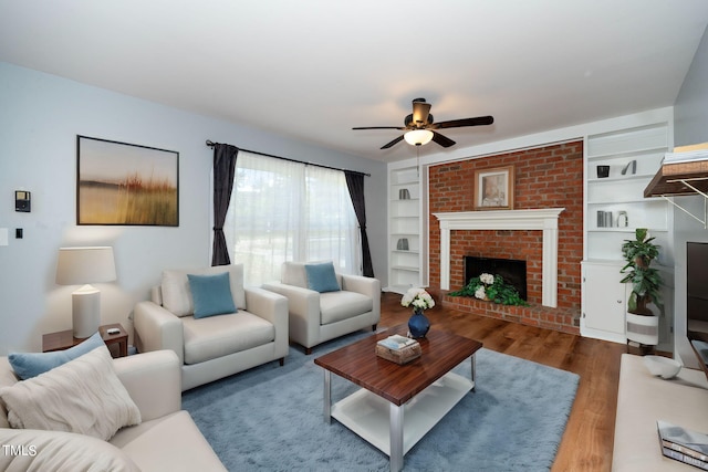 living room with hardwood / wood-style floors, ceiling fan, built in shelves, and a brick fireplace