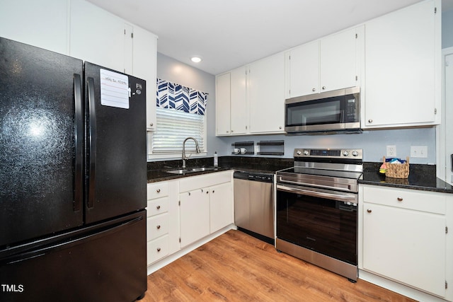 kitchen featuring appliances with stainless steel finishes, dark stone counters, sink, white cabinets, and light hardwood / wood-style floors