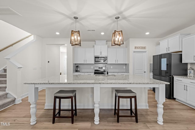 kitchen with appliances with stainless steel finishes, an island with sink, light stone counters, white cabinetry, and decorative light fixtures