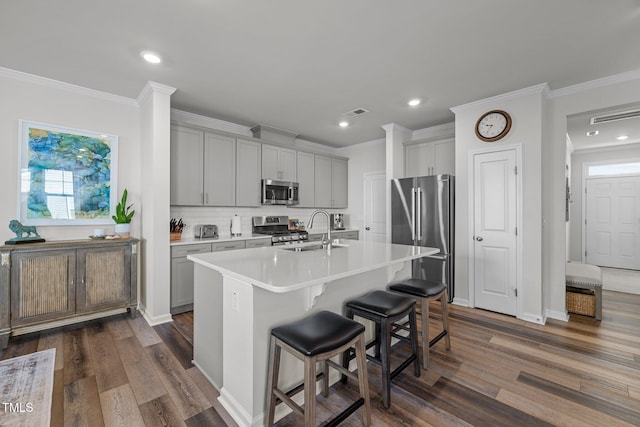 kitchen with stainless steel appliances, dark wood-type flooring, sink, a center island with sink, and a breakfast bar area