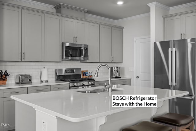 kitchen with appliances with stainless steel finishes, crown molding, sink, a center island with sink, and a breakfast bar area