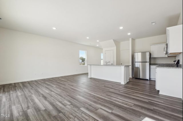 kitchen featuring a kitchen island with sink, stainless steel refrigerator, white cabinetry, and wood-type flooring