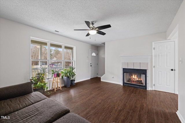 unfurnished living room featuring a tiled fireplace, ceiling fan, dark wood-type flooring, and a textured ceiling