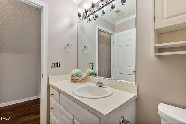 bathroom featuring vanity, hardwood / wood-style flooring, toilet, ornamental molding, and a textured ceiling