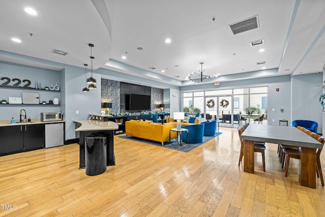 interior space with pendant lighting, light hardwood / wood-style floors, sink, and a tray ceiling