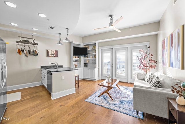 living room with built in shelves, ceiling fan, and light hardwood / wood-style floors