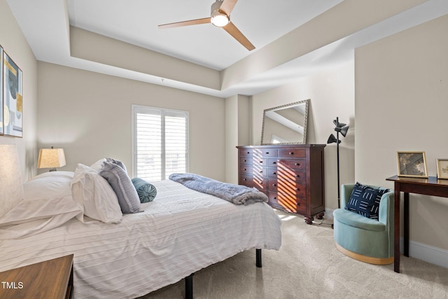 carpeted bedroom with ceiling fan and a raised ceiling