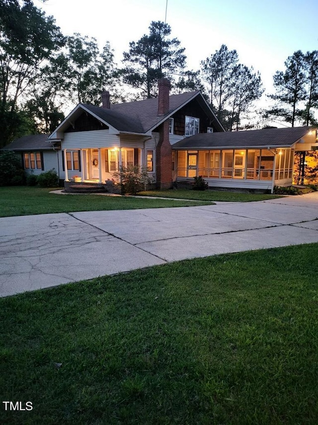 view of front of home with concrete driveway, a front yard, a sunroom, and a chimney