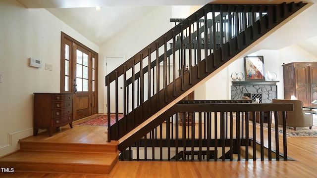 staircase with a fireplace, hardwood / wood-style flooring, and vaulted ceiling