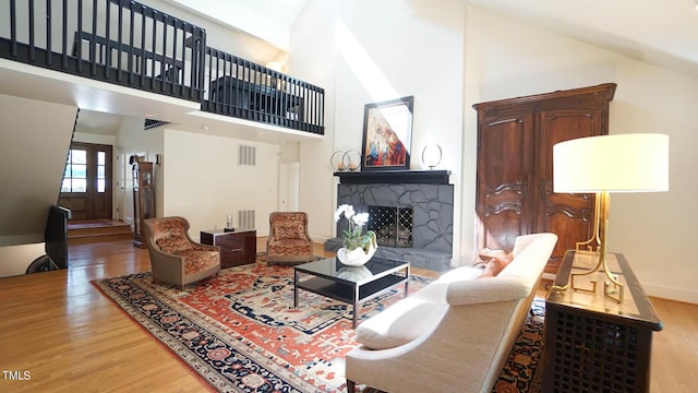 living room with wood-type flooring, a stone fireplace, and a high ceiling