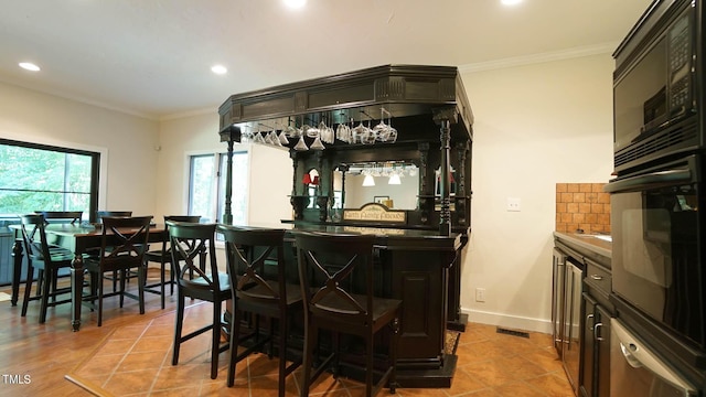 bar featuring black appliances, decorative backsplash, light tile patterned flooring, and crown molding