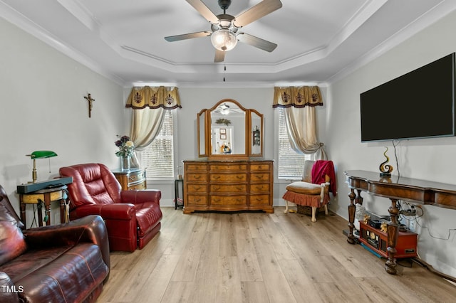 living area featuring a raised ceiling, light wood-type flooring, and ornamental molding