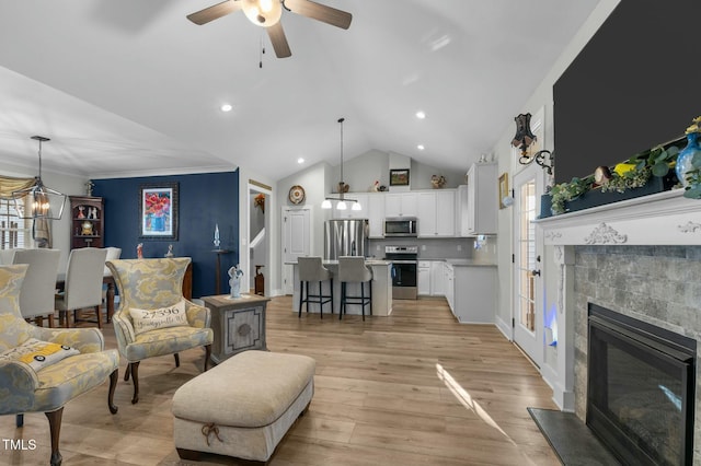 living room featuring crown molding, light hardwood / wood-style floors, vaulted ceiling, a fireplace, and ceiling fan with notable chandelier