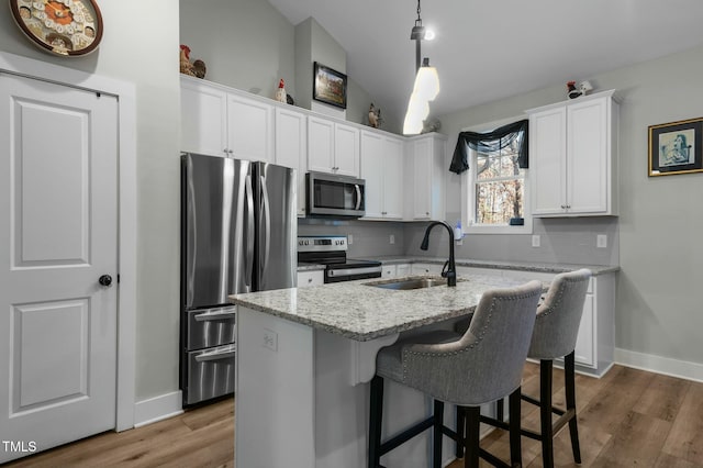 kitchen with light stone counters, stainless steel appliances, sink, white cabinetry, and an island with sink