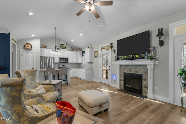 living room with ceiling fan, vaulted ceiling, a tile fireplace, and light hardwood / wood-style flooring