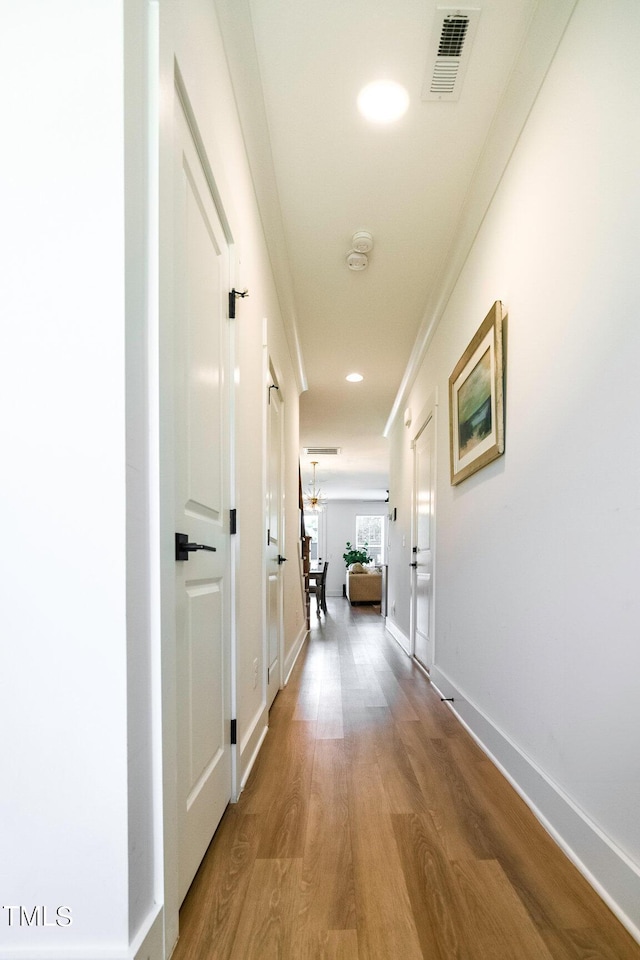 corridor with a chandelier, wood-type flooring, and crown molding