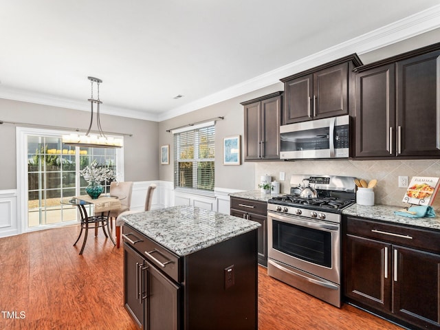 kitchen featuring pendant lighting, crown molding, appliances with stainless steel finishes, dark brown cabinets, and a kitchen island