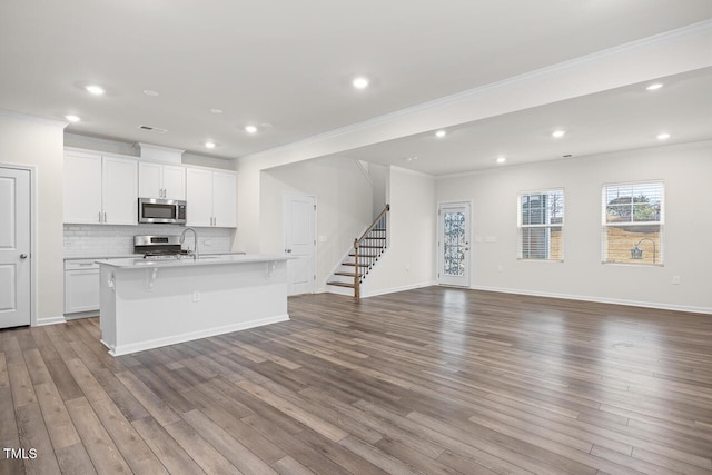 kitchen with a kitchen bar, stainless steel appliances, a kitchen island with sink, crown molding, and white cabinetry