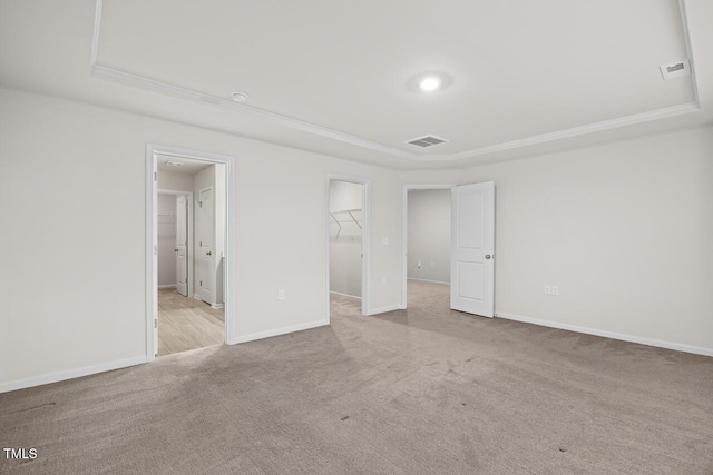 unfurnished bedroom featuring a raised ceiling, a spacious closet, a closet, and light colored carpet