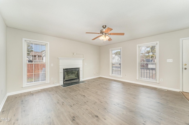 unfurnished living room with ceiling fan, a textured ceiling, a healthy amount of sunlight, and light wood-type flooring