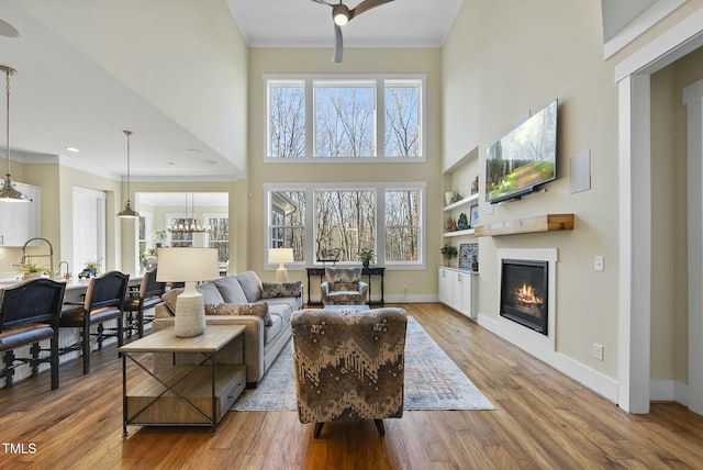 living room featuring built in shelves, ceiling fan, light hardwood / wood-style flooring, and a high ceiling