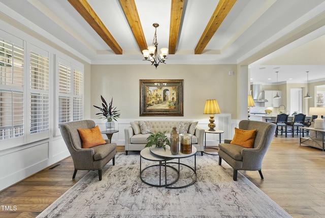 living room featuring beam ceiling, light wood-type flooring, and a notable chandelier