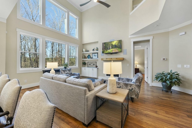 living room featuring wood-type flooring, ornamental molding, ceiling fan, and built in shelves