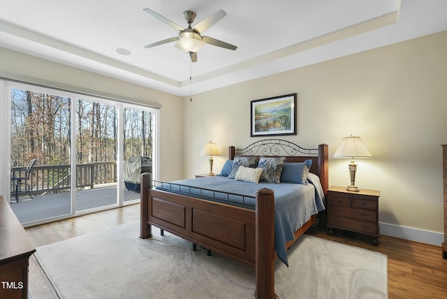 bedroom with light wood-type flooring, access to outside, a raised ceiling, and ceiling fan