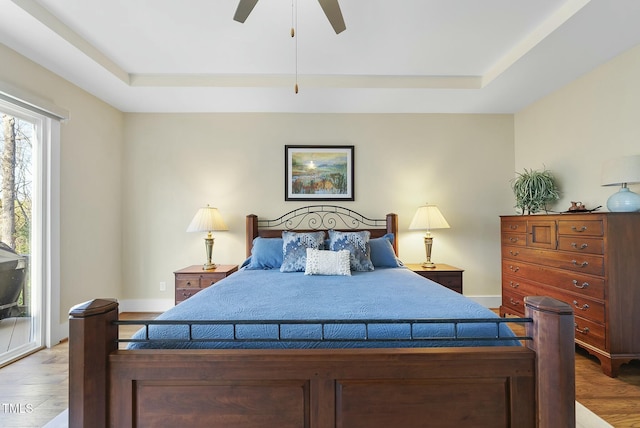 bedroom with wood-type flooring, access to outside, a raised ceiling, and ceiling fan