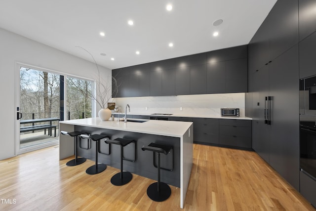 kitchen with sink, backsplash, a spacious island, light hardwood / wood-style floors, and a kitchen bar