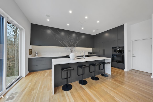 kitchen with a spacious island, sink, light wood-type flooring, a kitchen breakfast bar, and decorative backsplash