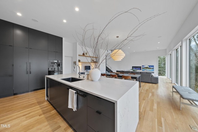 kitchen with sink, a large island with sink, dishwasher, and light wood-type flooring