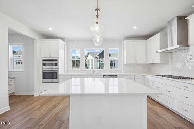 kitchen with stainless steel appliances, hanging light fixtures, white cabinets, wall chimney range hood, and backsplash