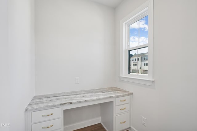 unfurnished office featuring built in desk and dark hardwood / wood-style floors