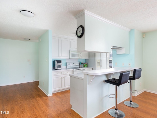 kitchen with light countertops, white cabinetry, white appliances, a peninsula, and a kitchen breakfast bar