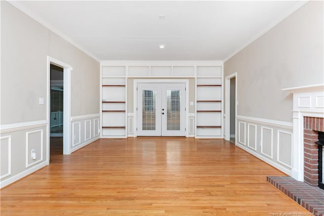 unfurnished living room featuring a fireplace, light wood-type flooring, french doors, and ornamental molding