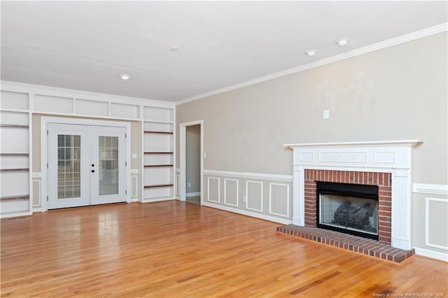 unfurnished living room with french doors, a brick fireplace, built in features, light hardwood / wood-style flooring, and crown molding