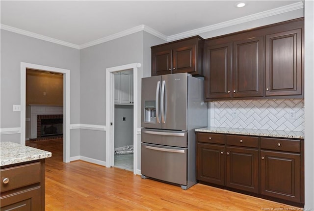 kitchen with decorative backsplash, stainless steel fridge, light stone countertops, crown molding, and a fireplace