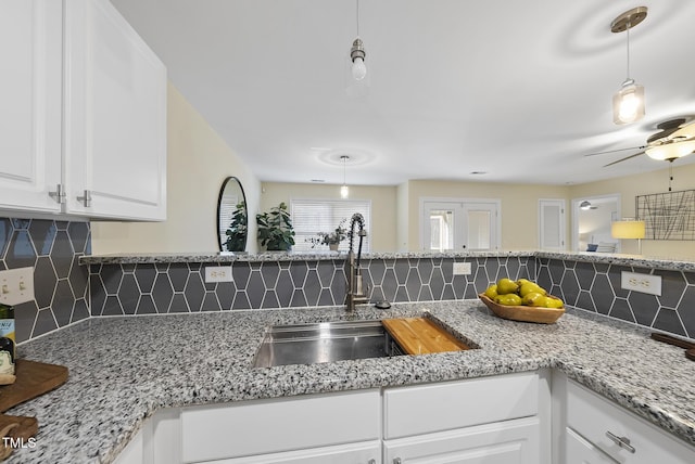 kitchen with ceiling fan, sink, hanging light fixtures, decorative backsplash, and white cabinets