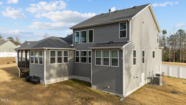 rear view of property featuring a shingled roof, central AC, fence, and a lawn