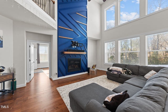 living area with a large fireplace, dark wood finished floors, a towering ceiling, and baseboards