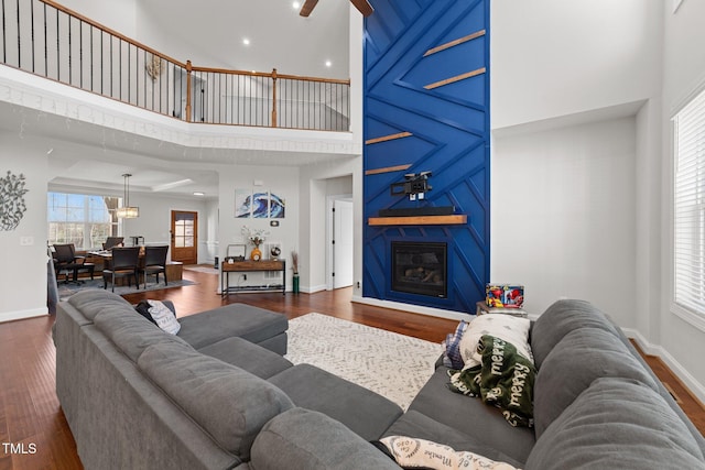 living room with a large fireplace, a high ceiling, wood finished floors, and a ceiling fan