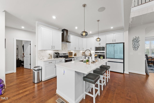 kitchen featuring built in appliances, a sink, light countertops, wall chimney exhaust hood, and tasteful backsplash