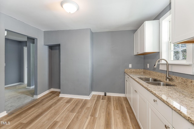 kitchen featuring white cabinets, light hardwood / wood-style floors, light stone counters, and sink