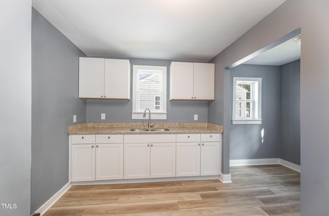 kitchen with white cabinets, light hardwood / wood-style floors, light stone counters, and sink