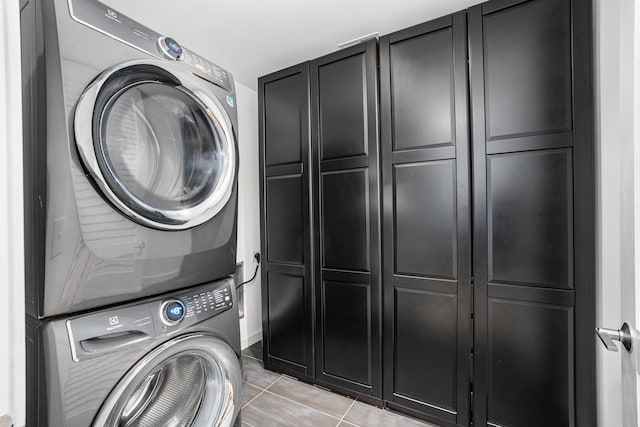 washroom featuring stacked washer / dryer, light tile patterned floors, and cabinets