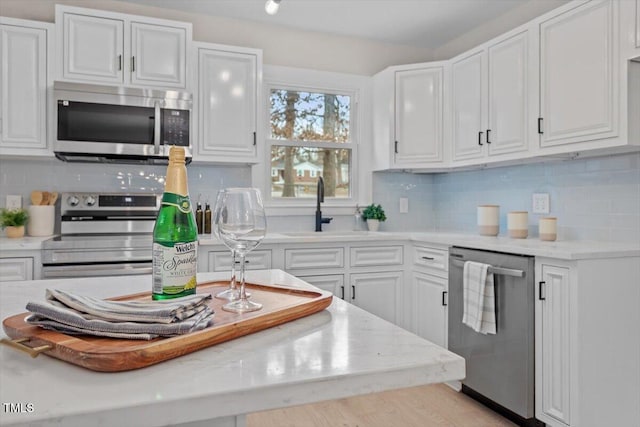 kitchen with sink, white cabinetry, stainless steel appliances, light stone counters, and decorative backsplash