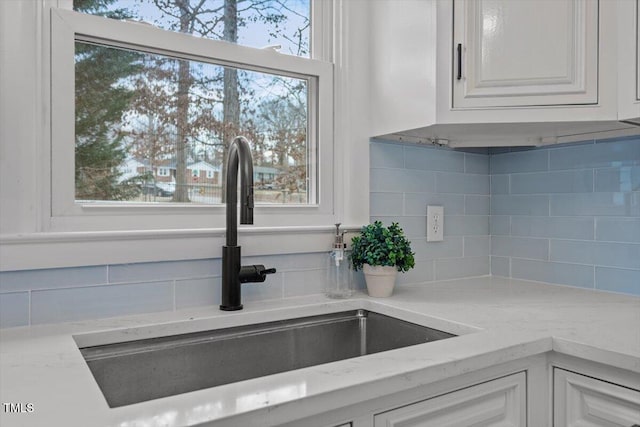 interior details with white cabinetry, light stone countertops, sink, and backsplash