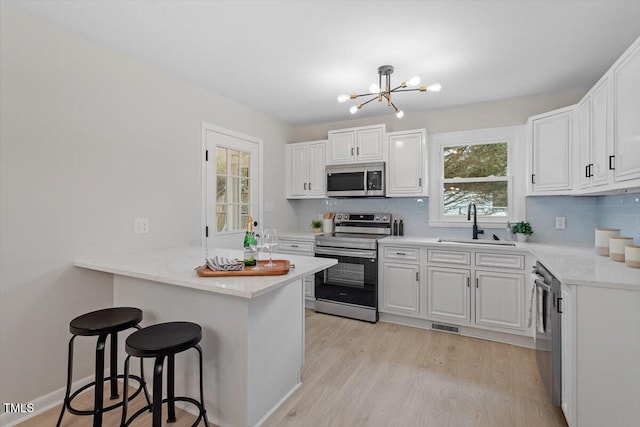 kitchen featuring sink, appliances with stainless steel finishes, white cabinetry, a kitchen breakfast bar, and kitchen peninsula